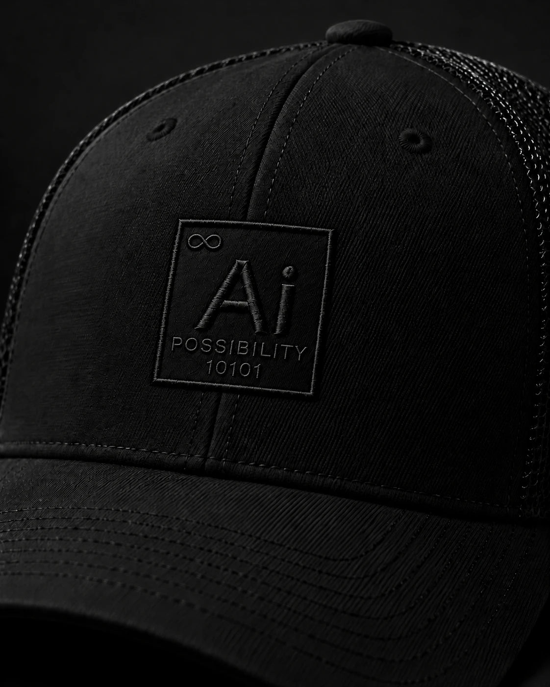 Close-up of the tone-on-tone embroidered Ai + You element tile on the front panel of the black Possibility Trucker Hat