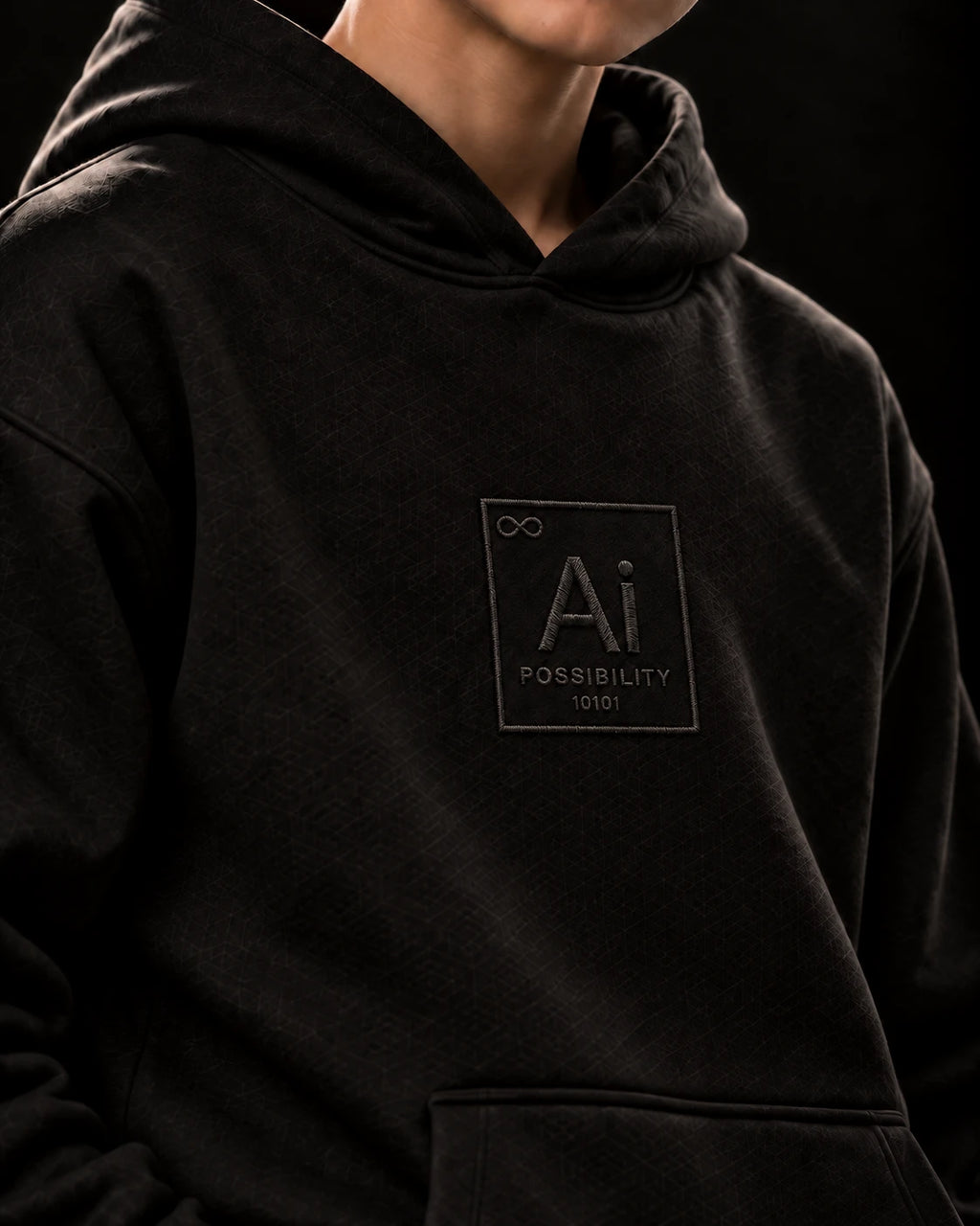 Close-up of the Ai + You element tile on the chest of the black Possibility Youth Hoodie